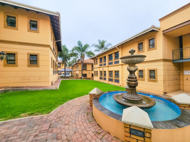 A well-maintained courtyard area featuring a central decorative fountain, paved pathways, and manicured lawn between office building wings.
