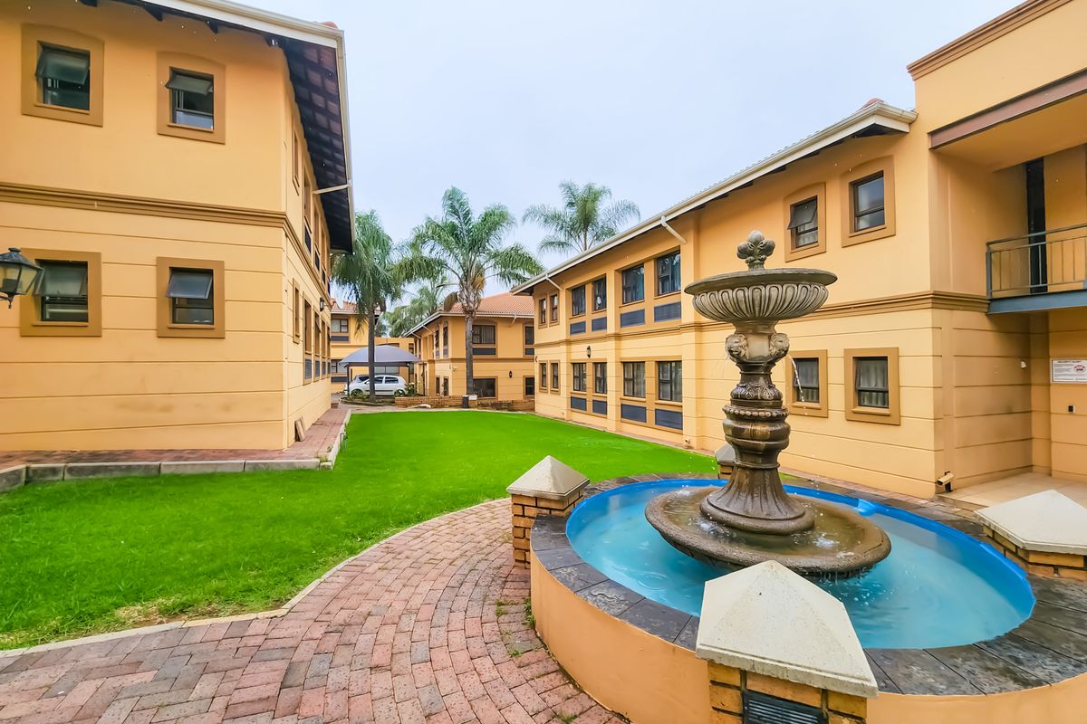 A well-maintained courtyard area featuring a central decorative fountain, paved pathways, and manicured lawn between office building wings.