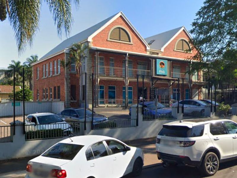 Front exterior view of a two-story brick commercial building featuring a metal roof, arched windows, and a fenced parking area.