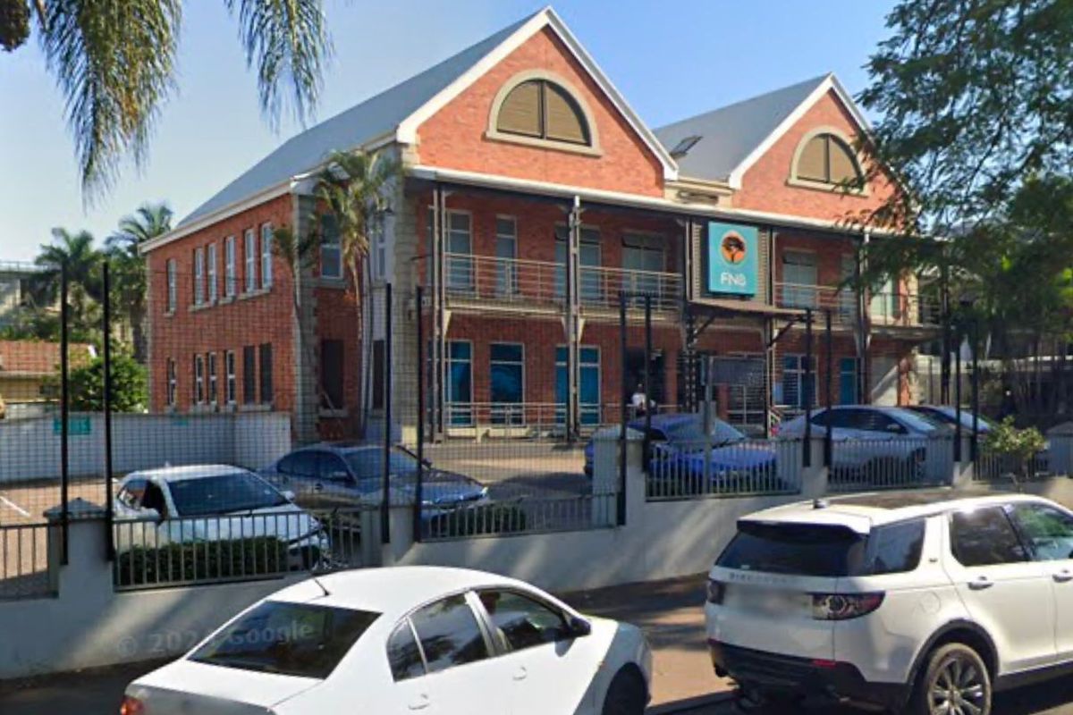 Front exterior view of a two-story brick commercial building featuring a metal roof, arched windows, and a fenced parking area.