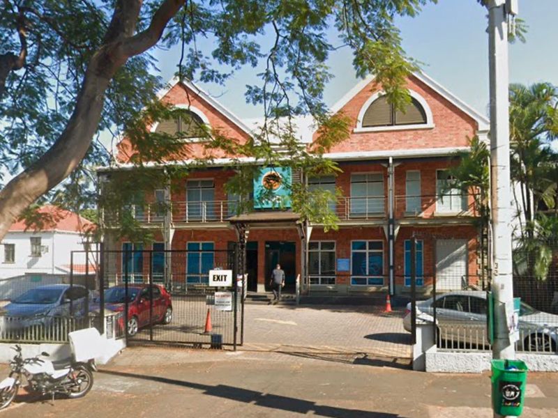 Front elevation of a multi-story brick commercial building featuring arched windows, metal balcony railings, and a paved entrance area with security gate.