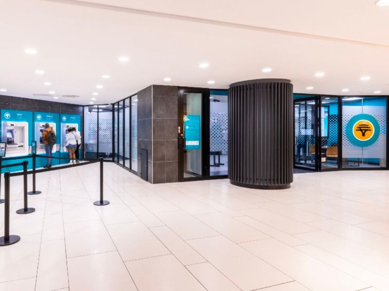 Modern retail banking lobby featuring tiled flooring, recessed lighting, glass partitions, and integrated ATM stations within a clean, professional environment.