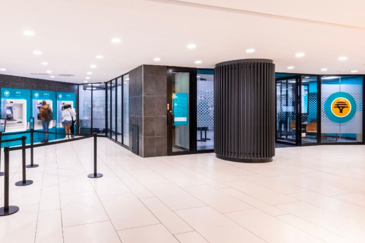 Modern retail banking lobby featuring tiled flooring, recessed lighting, glass partitions, and integrated ATM stations within a clean, professional environment.
