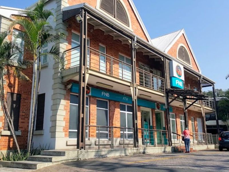 A well-maintained two-story brick commercial building featuring a balcony, paved frontage, and prominent signage, suitable for retail or office use.