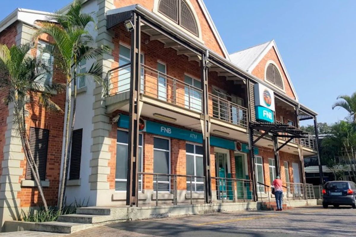 A well-maintained two-story brick commercial building featuring a balcony, paved frontage, and prominent signage, suitable for retail or office use.
