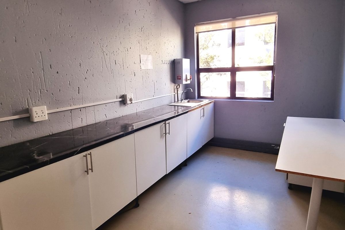 A functional office kitchenette featuring built-in cabinetry, a dark countertop, a stainless steel sink, and a wall-mounted water heater.