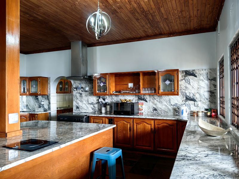 A spacious kitchen featuring wooden cabinetry, marble-look countertops, a built-in hob, stainless steel extractor fan, and a distinctive wooden ceiling.