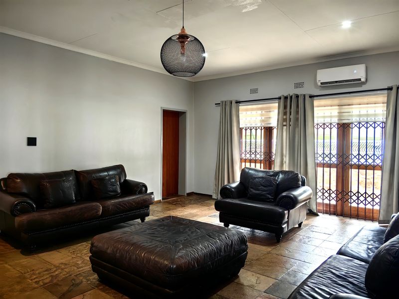 A spacious living room featuring tiled flooring, a split-system air conditioner, and large sliding glass doors with security gates for natural light and access.