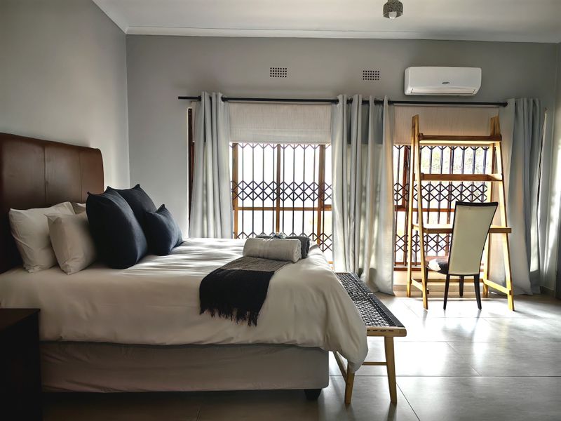 A well-maintained bedroom featuring tiled flooring, a wall-mounted air conditioning unit, and secure window gates, offering a clean and functional living space.