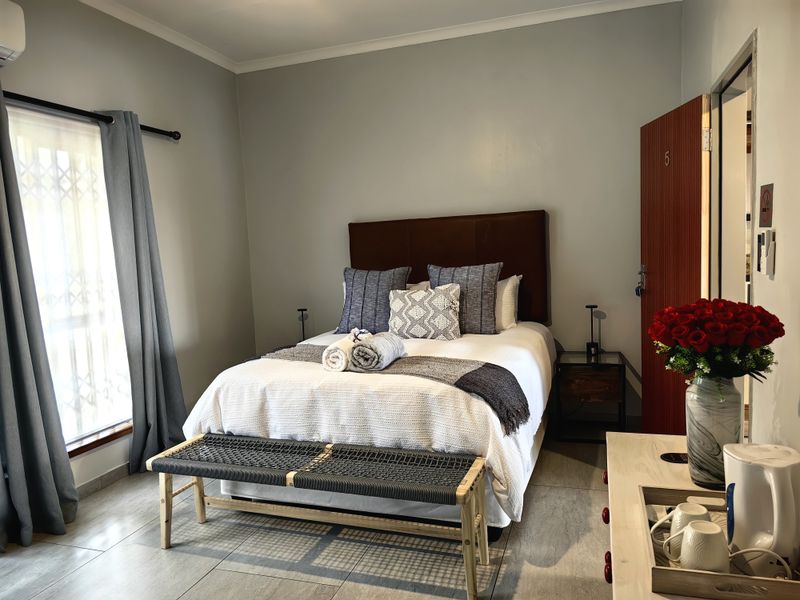 A well-maintained guest bedroom featuring tiled flooring, an air conditioning unit, and a secure window with a fitted security gate.