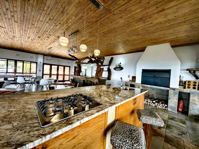 Spacious open-plan living and kitchen area featuring a large granite island with gas hob, wooden ceiling, and a built-in indoor fireplace.
