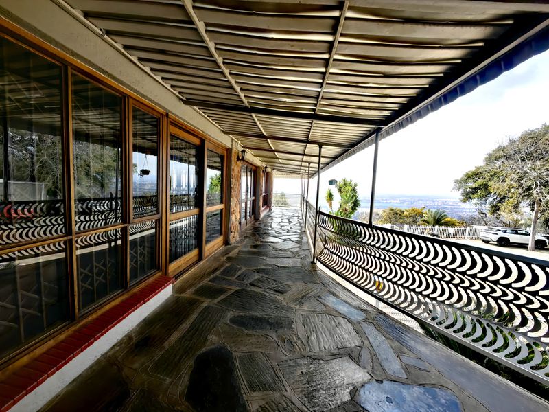 A spacious covered patio featuring stone flooring, decorative metal railings, and expansive sliding glass doors with scenic views.