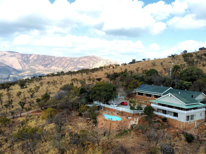 Aerial view of a guest house property situated on a hillside, featuring a swimming pool, expansive grounds, and scenic mountain views.