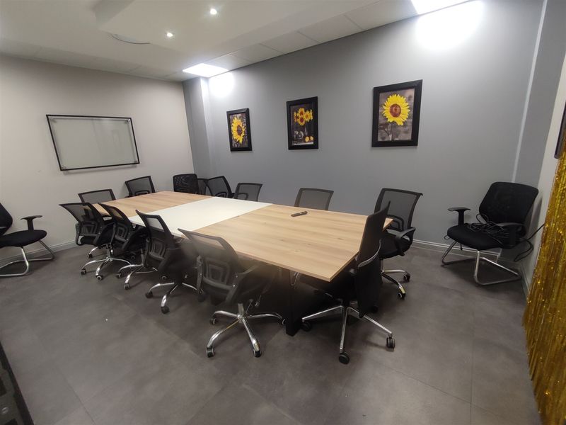 A professional office meeting room featuring tiled flooring, recessed ceiling lighting, and a wall-mounted whiteboard.