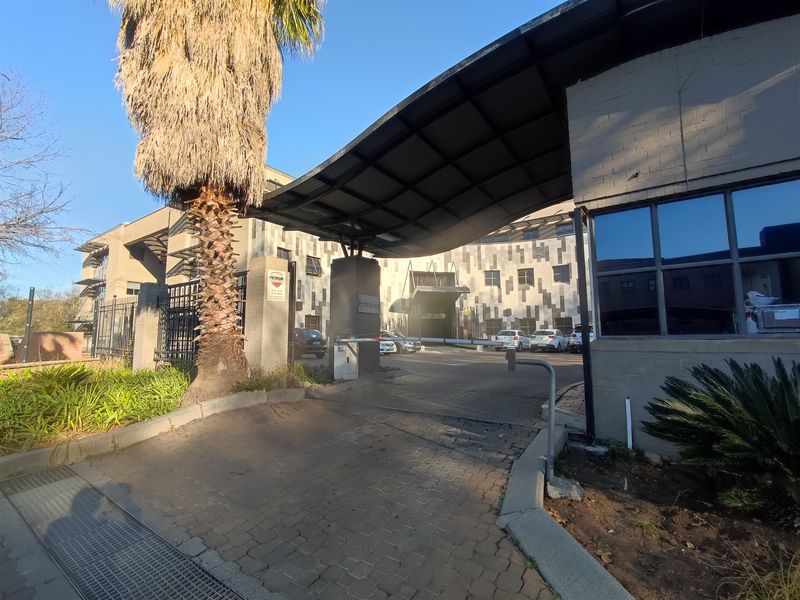 Front entrance view of the office building featuring a paved driveway, security boom gate, and a covered canopy structure.