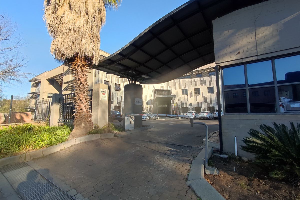 Front entrance view of the office building featuring a paved driveway, security boom gate, and a covered canopy structure.