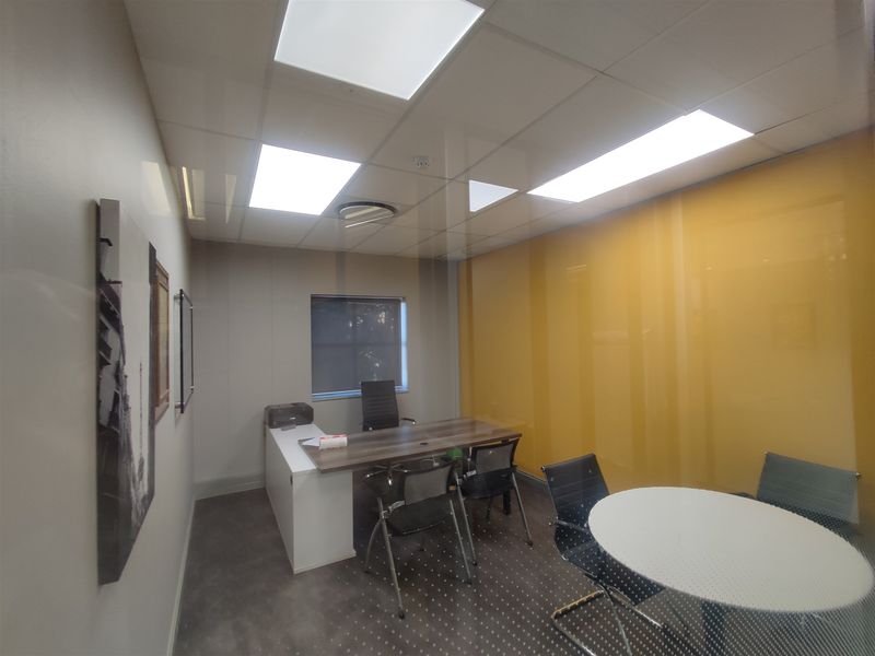 A modern, well-lit office space featuring a suspended ceiling with recessed lighting, a glass partition wall, and durable vinyl flooring.