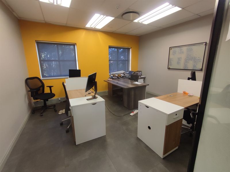 A functional office space featuring tiled flooring, recessed lighting, and large windows with roller blinds, providing a bright and professional work environment.