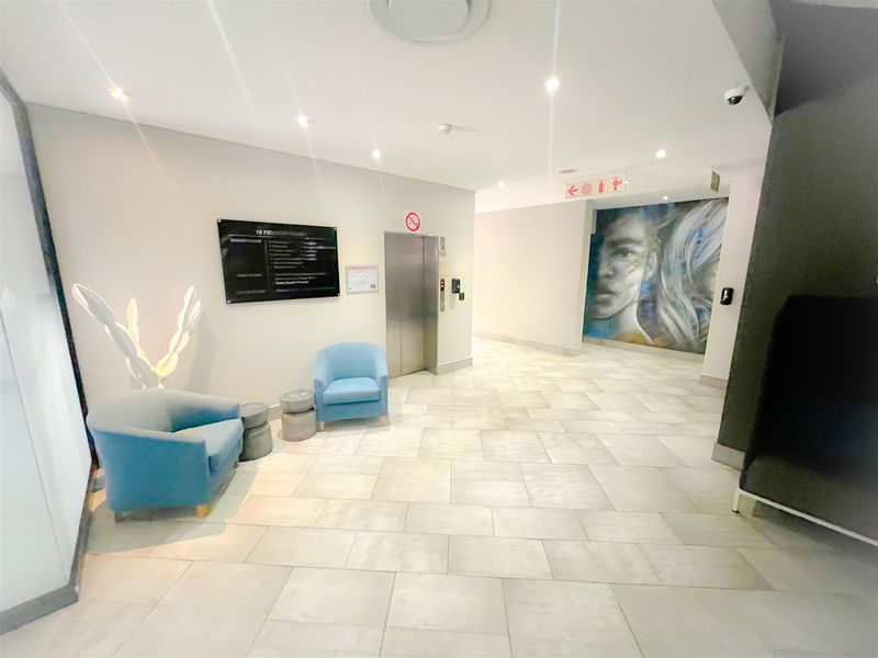 Modern office building lobby featuring tiled flooring, recessed lighting, a central elevator, and professional building directory signage.
