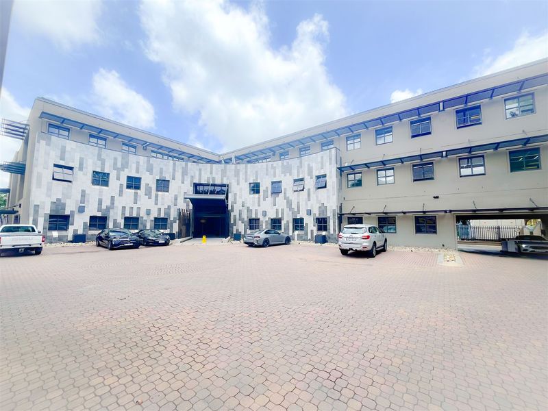 Modern office building exterior featuring a paved courtyard, stone-clad facade, and multiple windows, providing a professional and accessible entrance area.