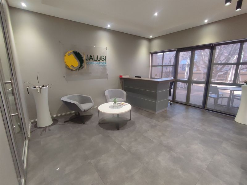 Modern office reception area featuring a built-in reception desk, tiled flooring, and large glass sliding doors providing natural light.