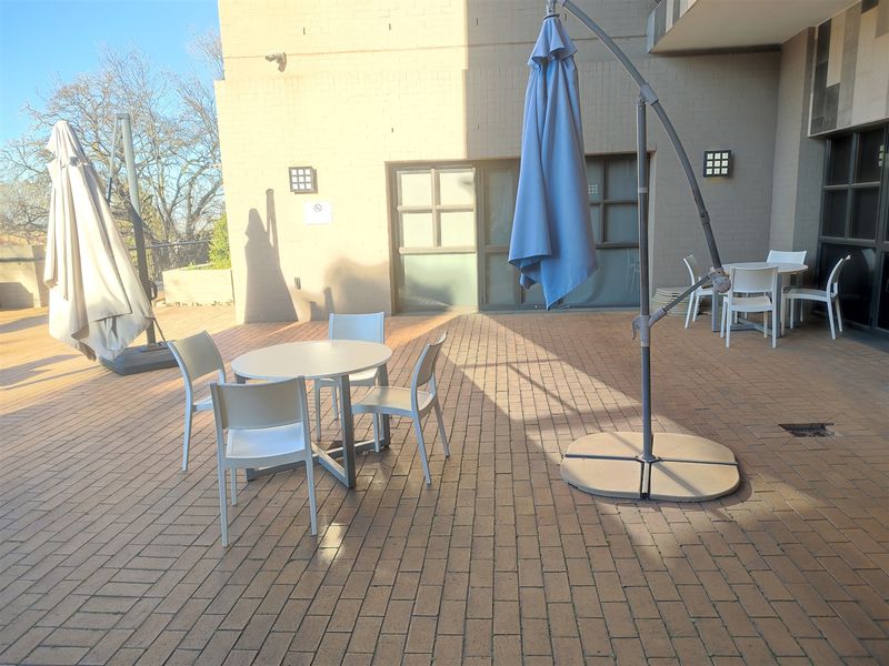 A spacious outdoor patio area featuring brick paving, exterior wall lighting, and access to the office building via sliding glass doors.