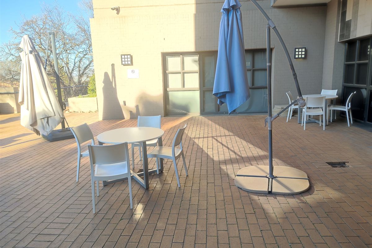 A spacious outdoor patio area featuring brick paving, exterior wall lighting, and access to the office building via sliding glass doors.