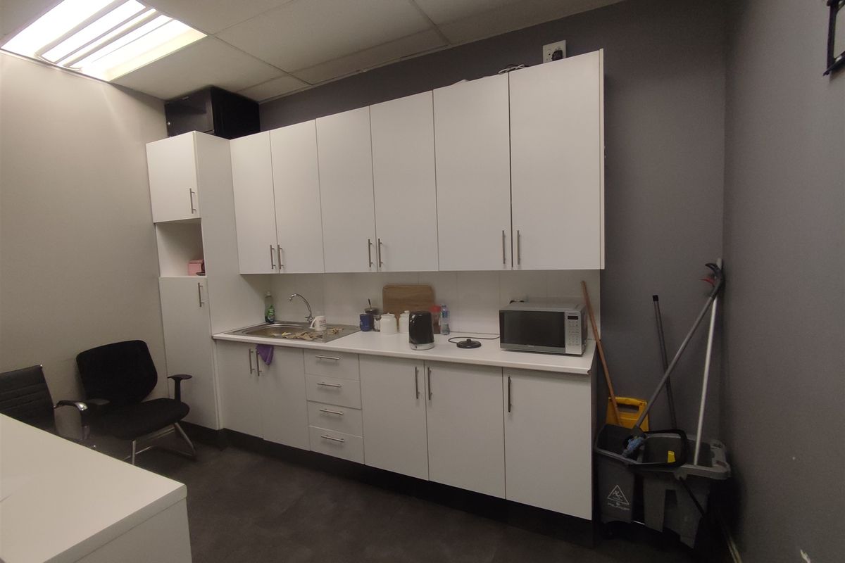 A functional office kitchenette featuring white built-in cabinetry, a stainless steel sink, and a laminate countertop, providing essential utility for the workspace.
