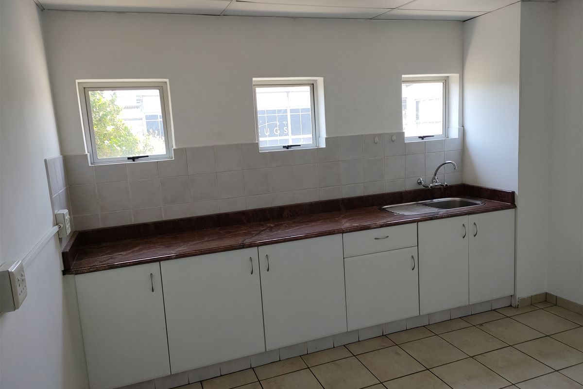 A functional kitchenette area featuring white cabinetry, a dark laminate countertop, a stainless steel sink, and tiled flooring.