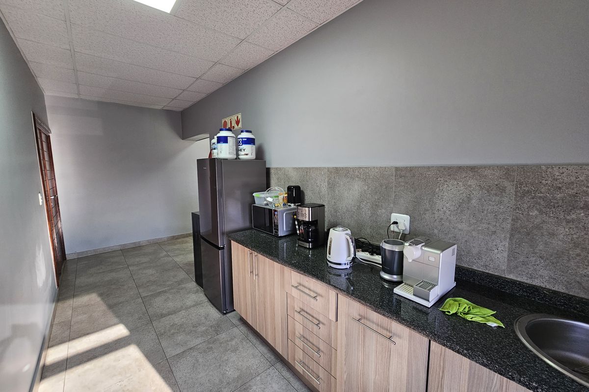 A functional kitchenette area featuring granite countertops, wood-finish cabinetry, a stainless steel sink, and a drop ceiling with integrated lighting.
