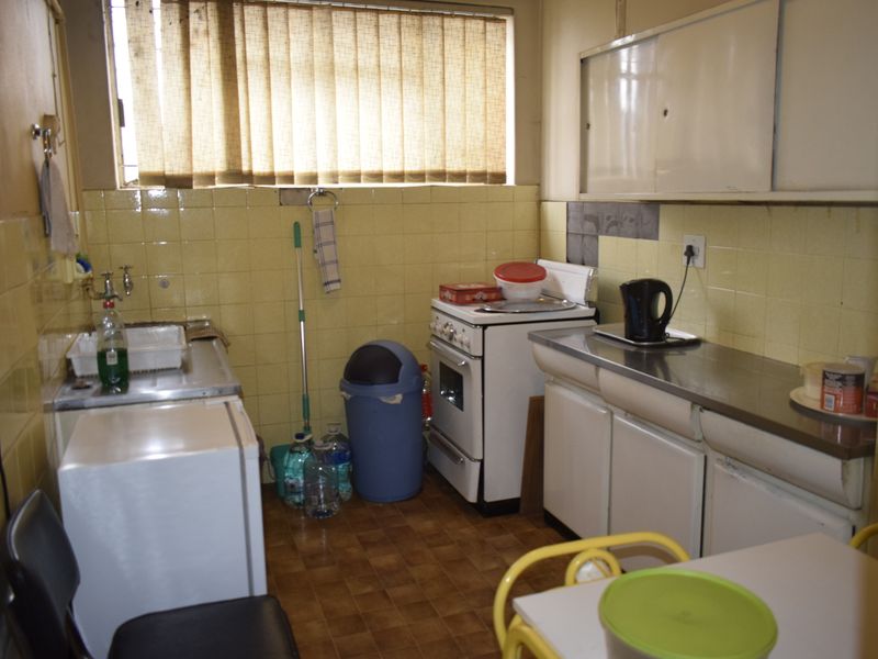 A compact, dated kitchen featuring original tiled splashbacks, stainless steel sink, and built-in cabinetry, offering significant potential for modernization and renovation.