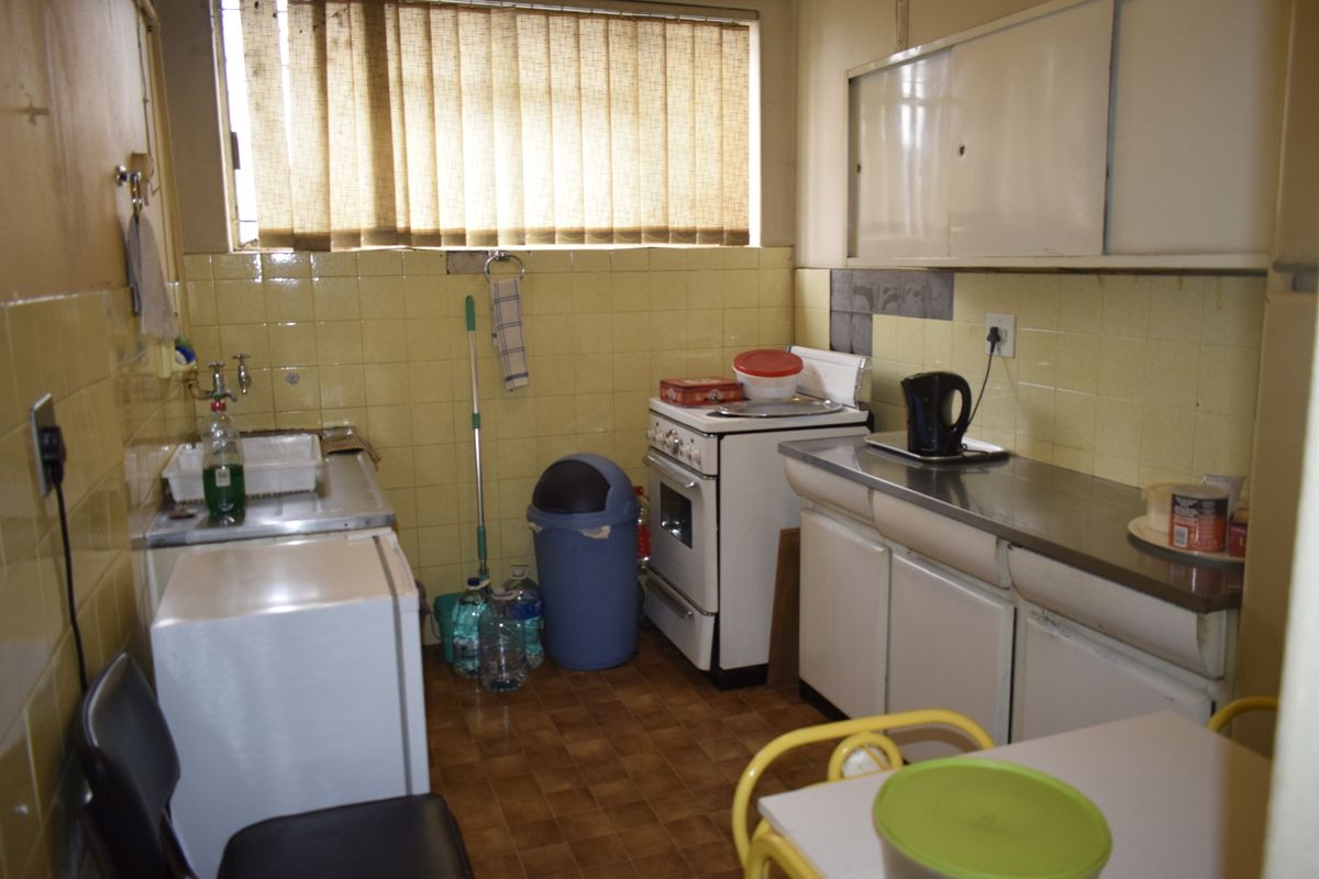 A compact, dated kitchen featuring original tiled splashbacks, stainless steel sink, and built-in cabinetry, offering significant potential for modernization and renovation.