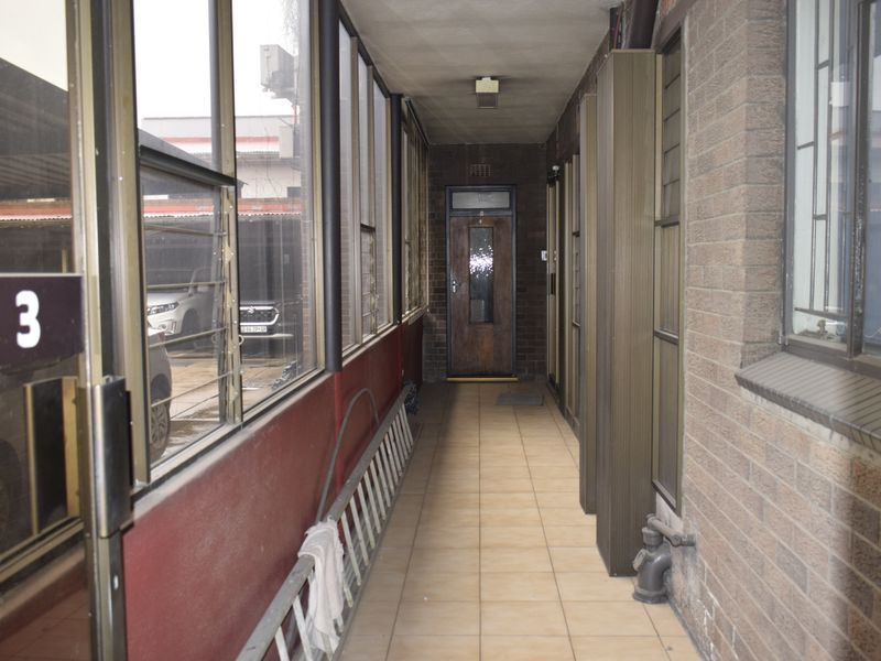 A functional office hallway featuring tiled flooring, brick walls, and aluminium-framed windows leading to an office entrance.