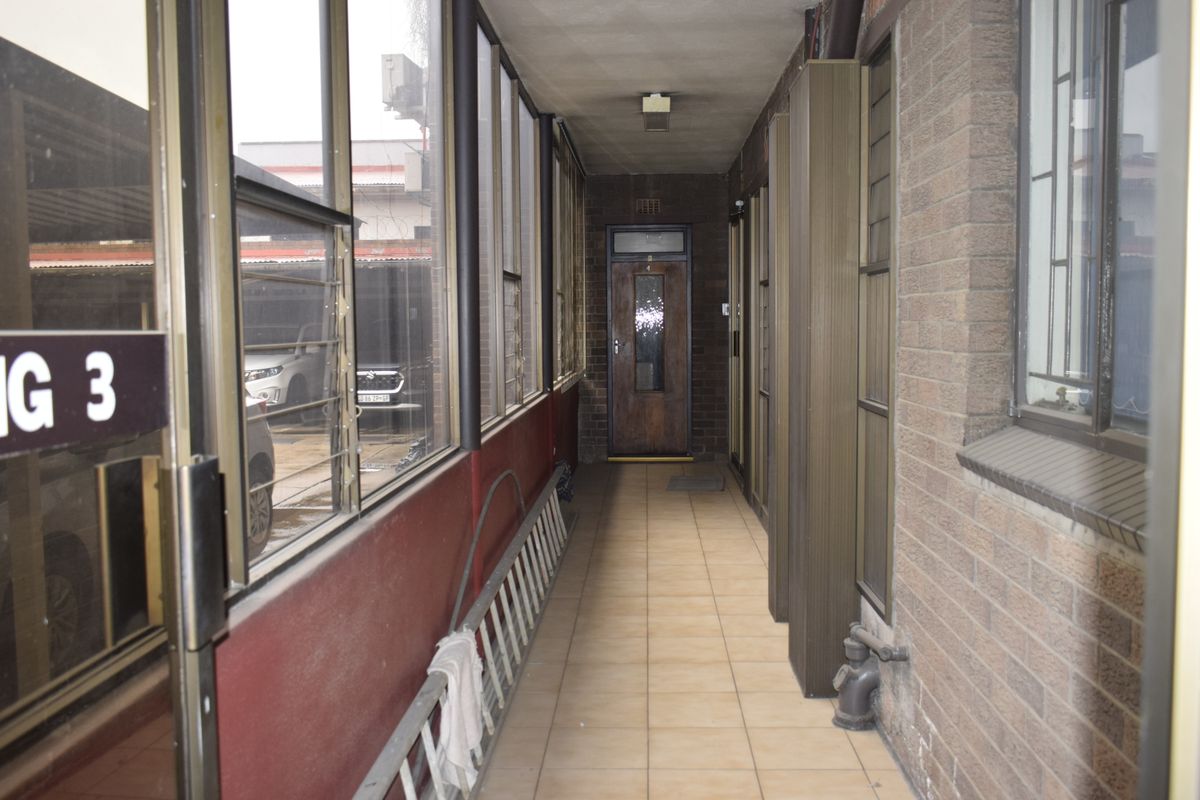 A functional office hallway featuring tiled flooring, brick walls, and aluminium-framed windows leading to an office entrance.