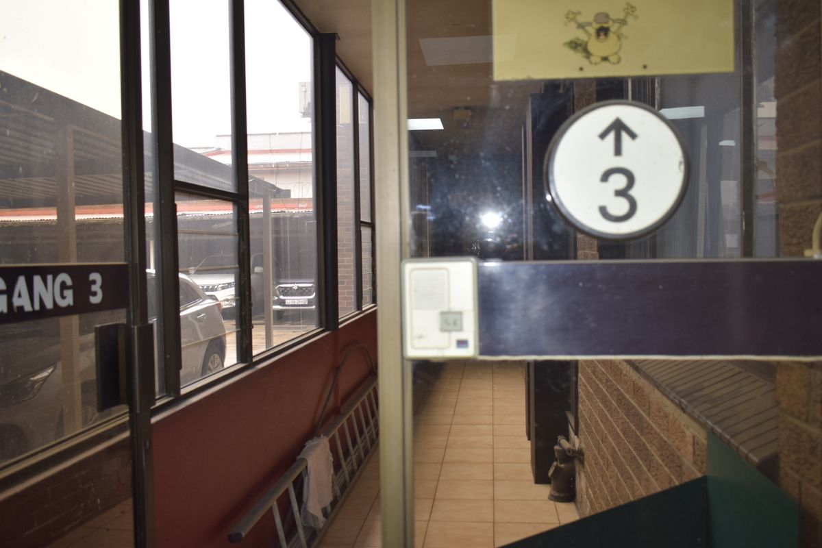 A functional office hallway featuring tiled flooring, brick wall accents, and large windows overlooking the parking area.