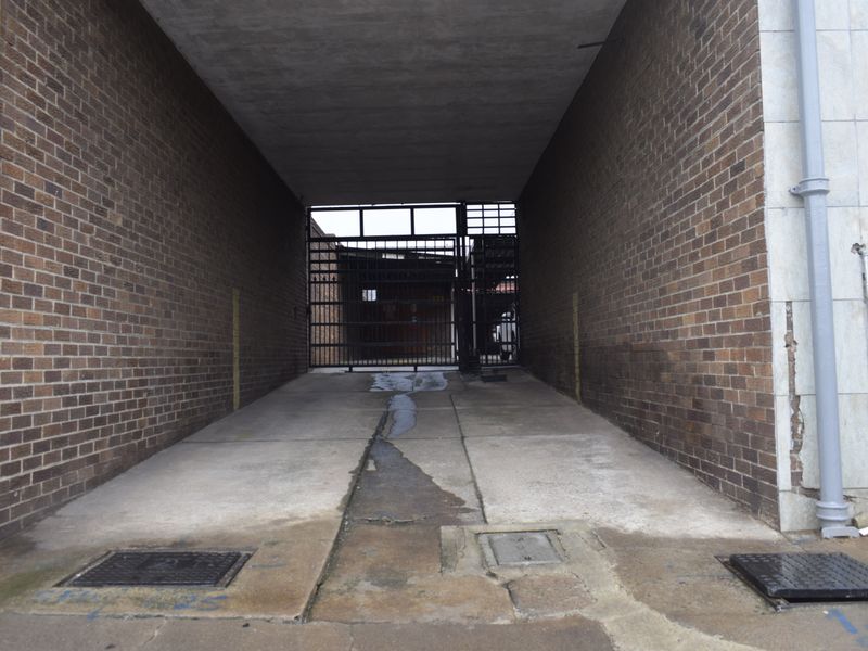 A covered rear access passage featuring brick walls, a concrete driveway with drainage, and a secure metal gate at the end.