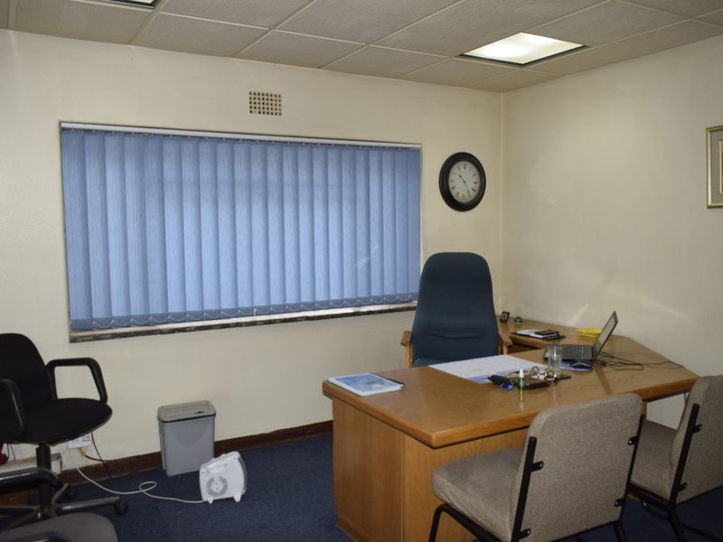 A functional office space featuring a suspended ceiling, recessed lighting, blue carpet flooring, and vertical blinds over the window.