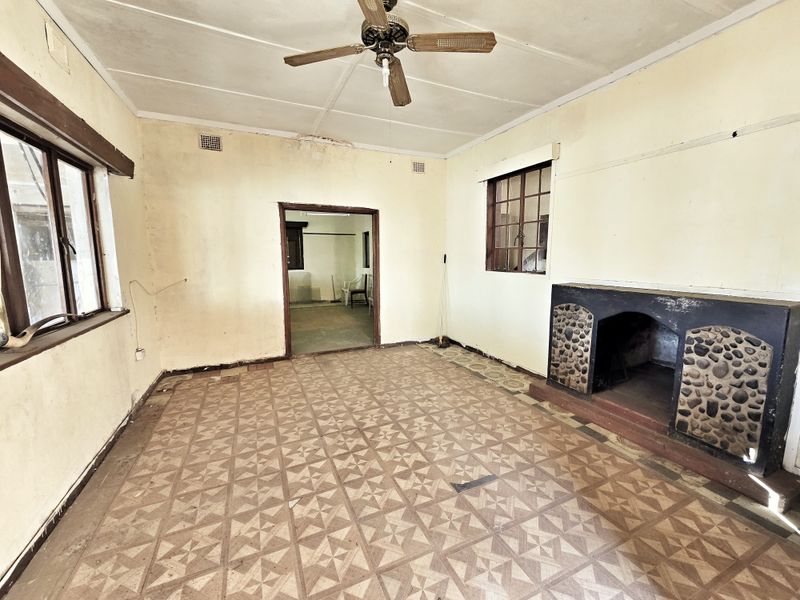 An empty living room featuring a stone-accented fireplace, ceiling fan, and patterned floor tiles, requiring significant renovation and cosmetic updates.