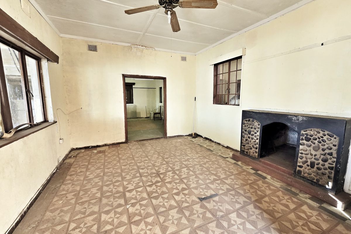 An empty living room featuring a stone-accented fireplace, ceiling fan, and patterned floor tiles, requiring significant renovation and cosmetic updates.