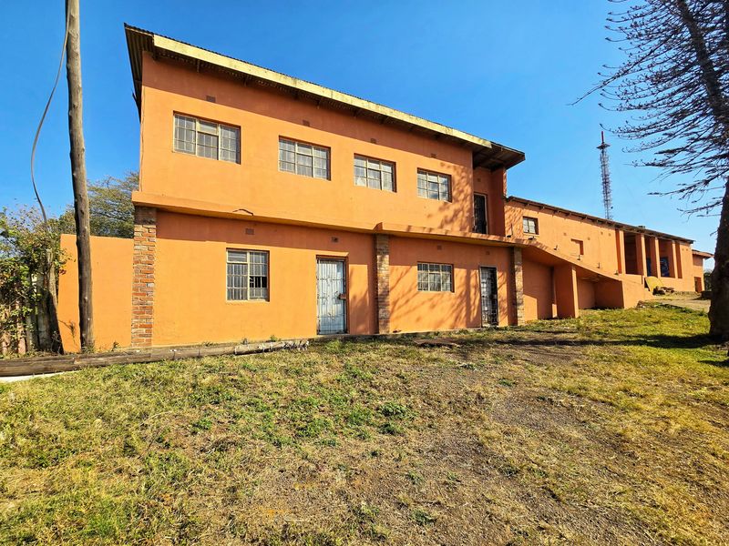 Rear exterior view of a two-story commercial building featuring orange painted plaster walls, steel-framed windows, and security gates.