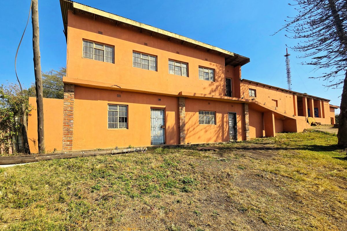 Rear exterior view of a two-story commercial building featuring orange painted plaster walls, steel-framed windows, and security gates.