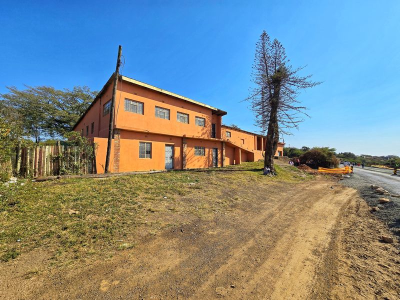 Exterior view of a two-story commercial building featuring orange plaster finish, steel-framed windows, and security access points, situated along a roadside.