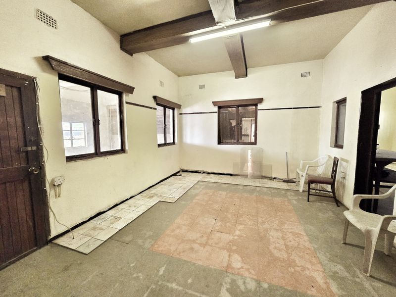 An empty commercial interior space featuring exposed timber ceiling beams, tiled flooring, and timber window frames, requiring renovation to improve its overall condition.