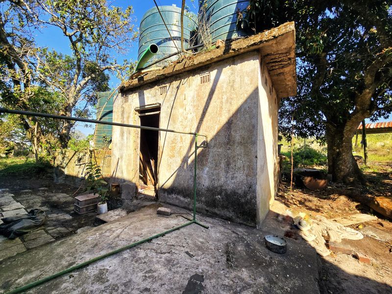 A detached concrete utility structure featuring external water storage tanks, showing significant signs of weathering and structural deterioration.