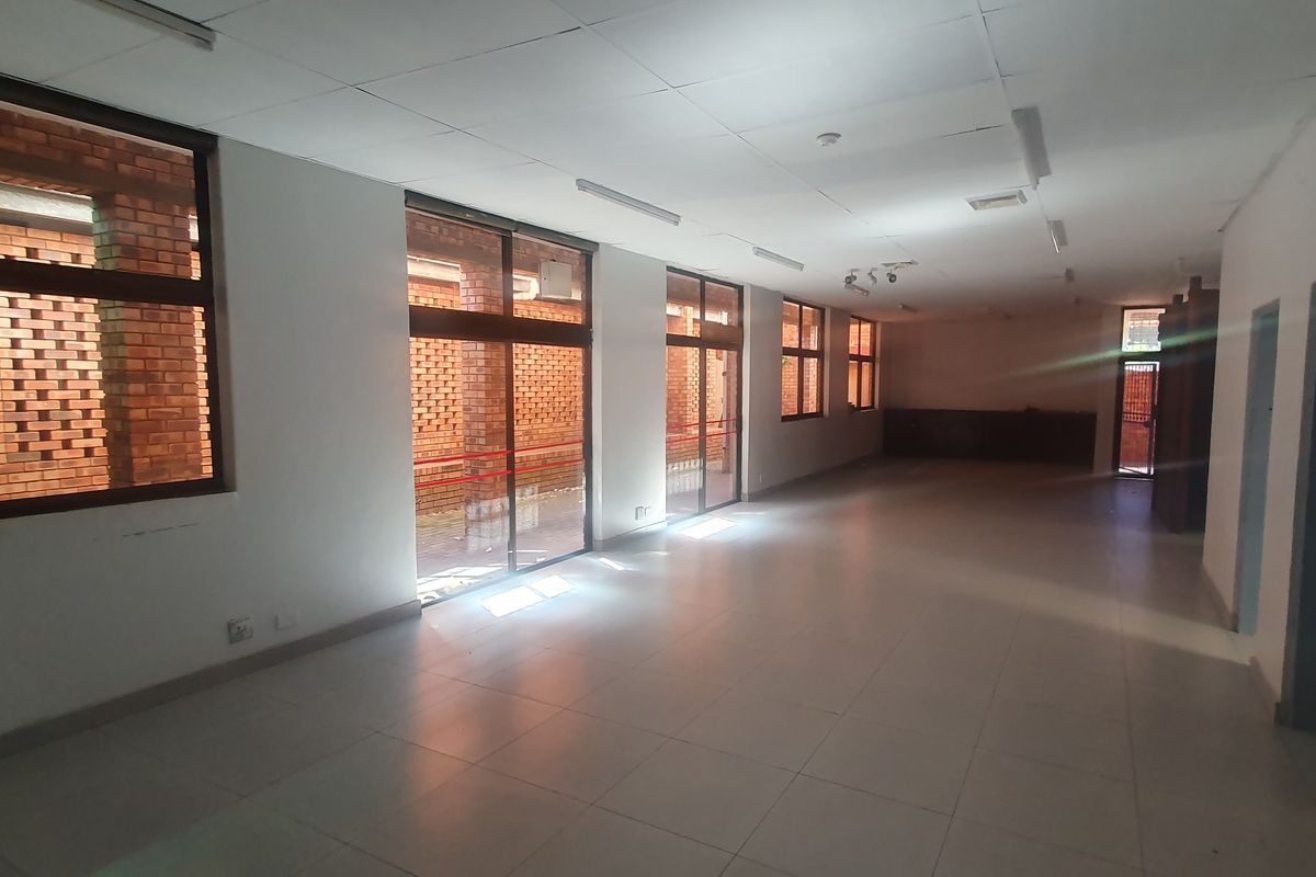 Spacious open-plan retail area featuring tiled flooring, ample natural light through large windows, and direct access to an exterior brick-walled courtyard.