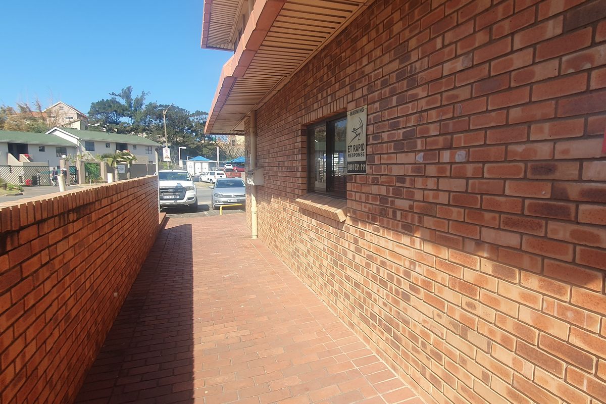 A paved exterior walkway alongside a brick building facade, featuring security signage and a perimeter brick wall.
