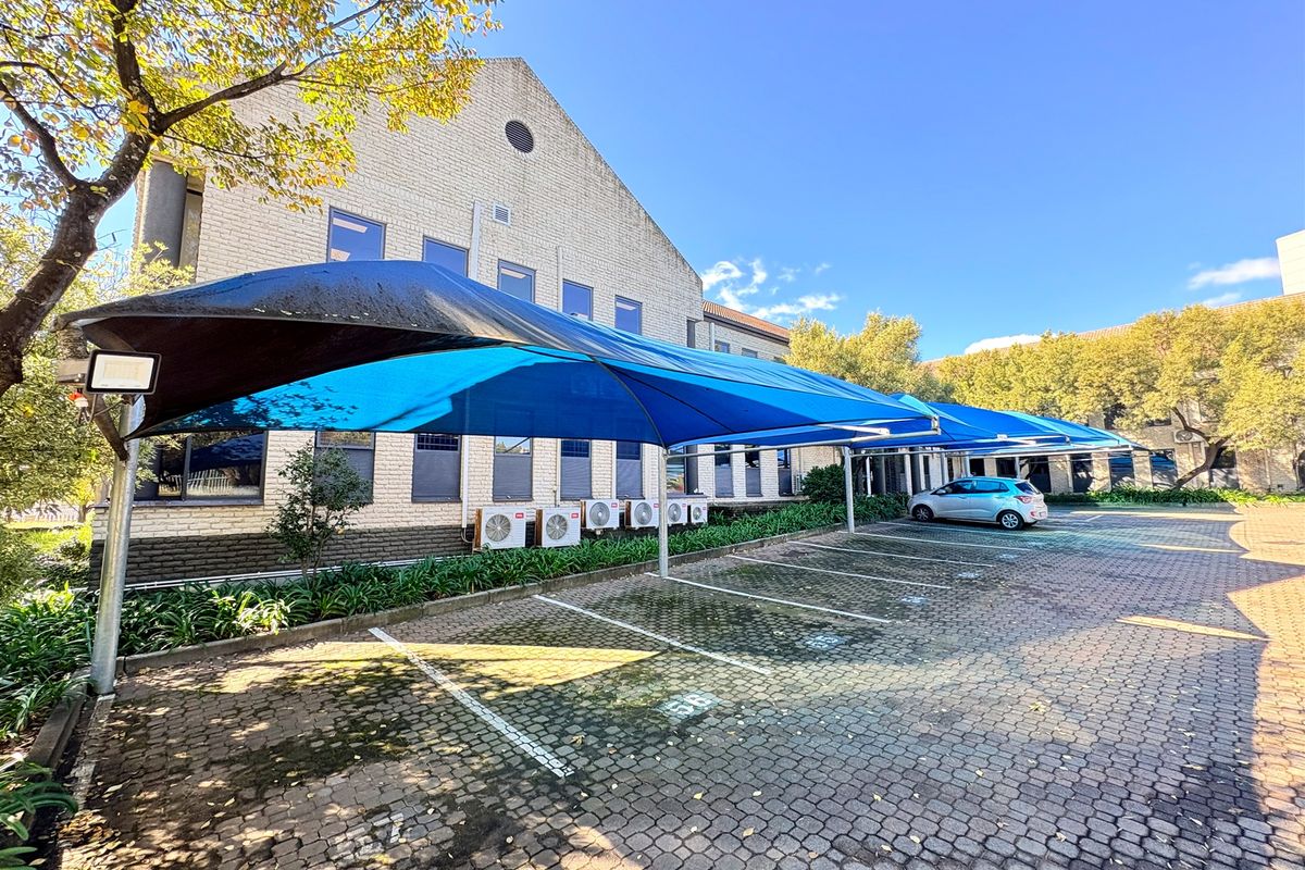 Exterior view of the office building featuring a paved parking area with blue shade-cloth carports and wall-mounted air conditioning units.