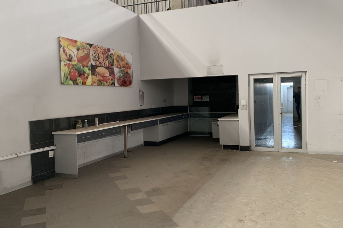 Industrial kitchen area featuring built-in cabinetry, tiled splashbacks, and double glass door access, suitable for food preparation or commercial utility use.