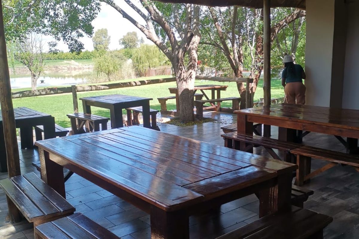 A covered outdoor patio area featuring a traditional thatched roof, timber support beams, and tiled flooring, overlooking a landscaped garden and pond.