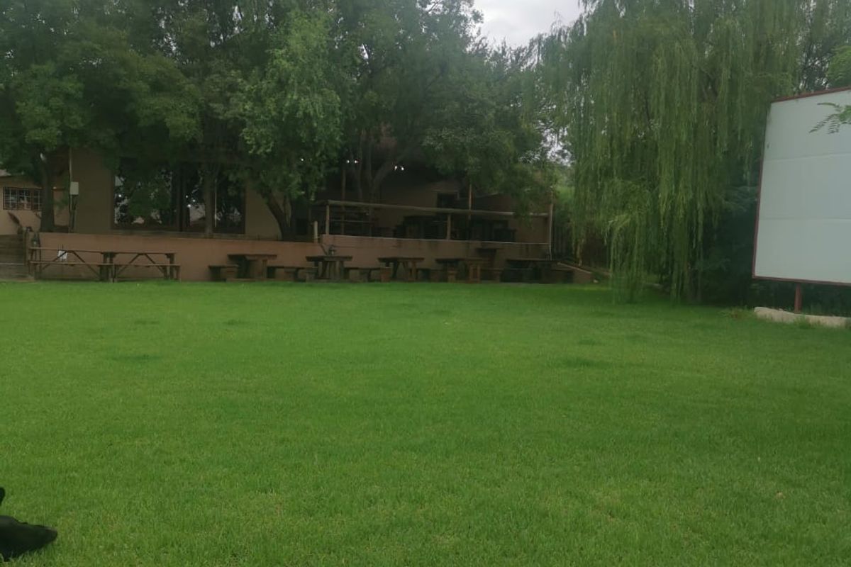 A view of the rear exterior area featuring a large landscaped lawn, stone retaining wall, and a large billboard structure.